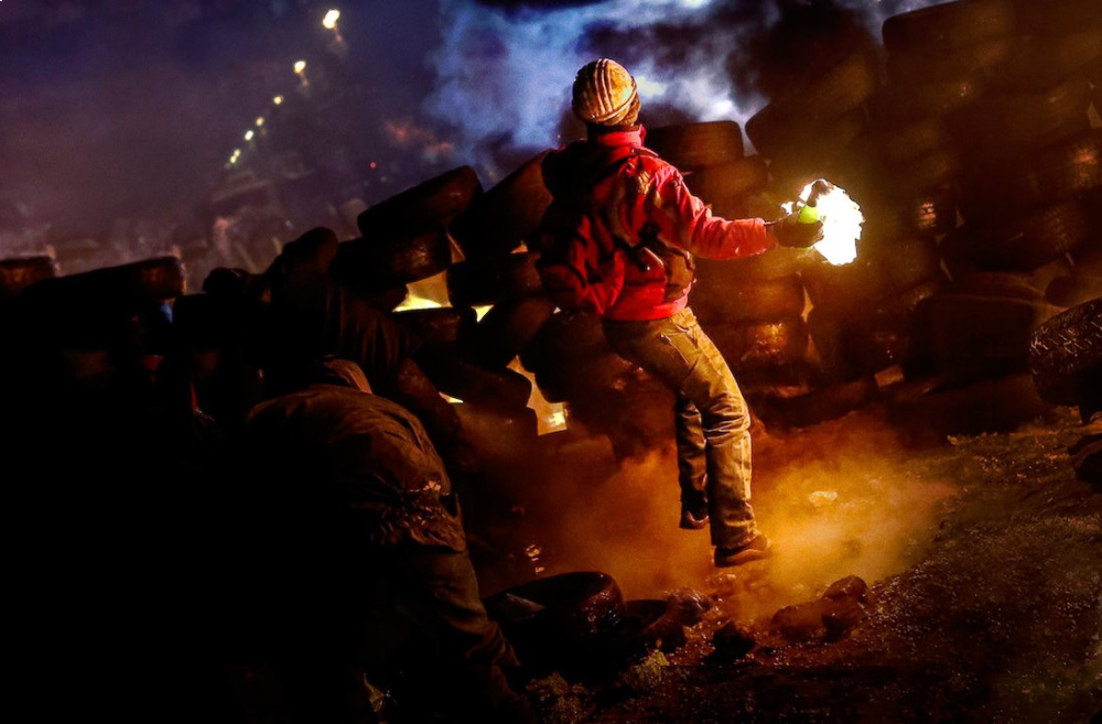 A nighttime shot of citizens fighting a police riot squad on the street.