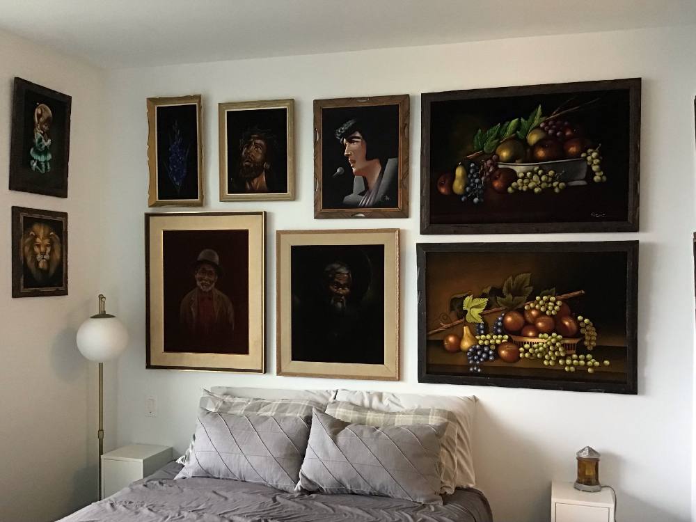 A bedroom with white walls, featuring eleven visible black velvet paintings.