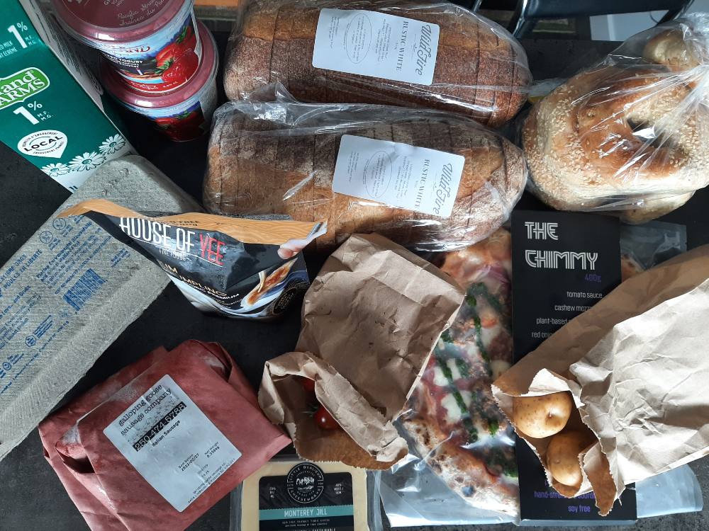 A bird&rsquo;s-eye view of a selection of groceries from For Good Measure in Victoria features two loaves of brown bread, a green carton of Island Farms milk, strawberry yogurt, a carton of eggs, and several packaged items to the bottom right corner of the frame.