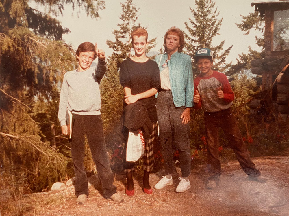 Four youth stand in a line, in various poses, looking directly at the camera.