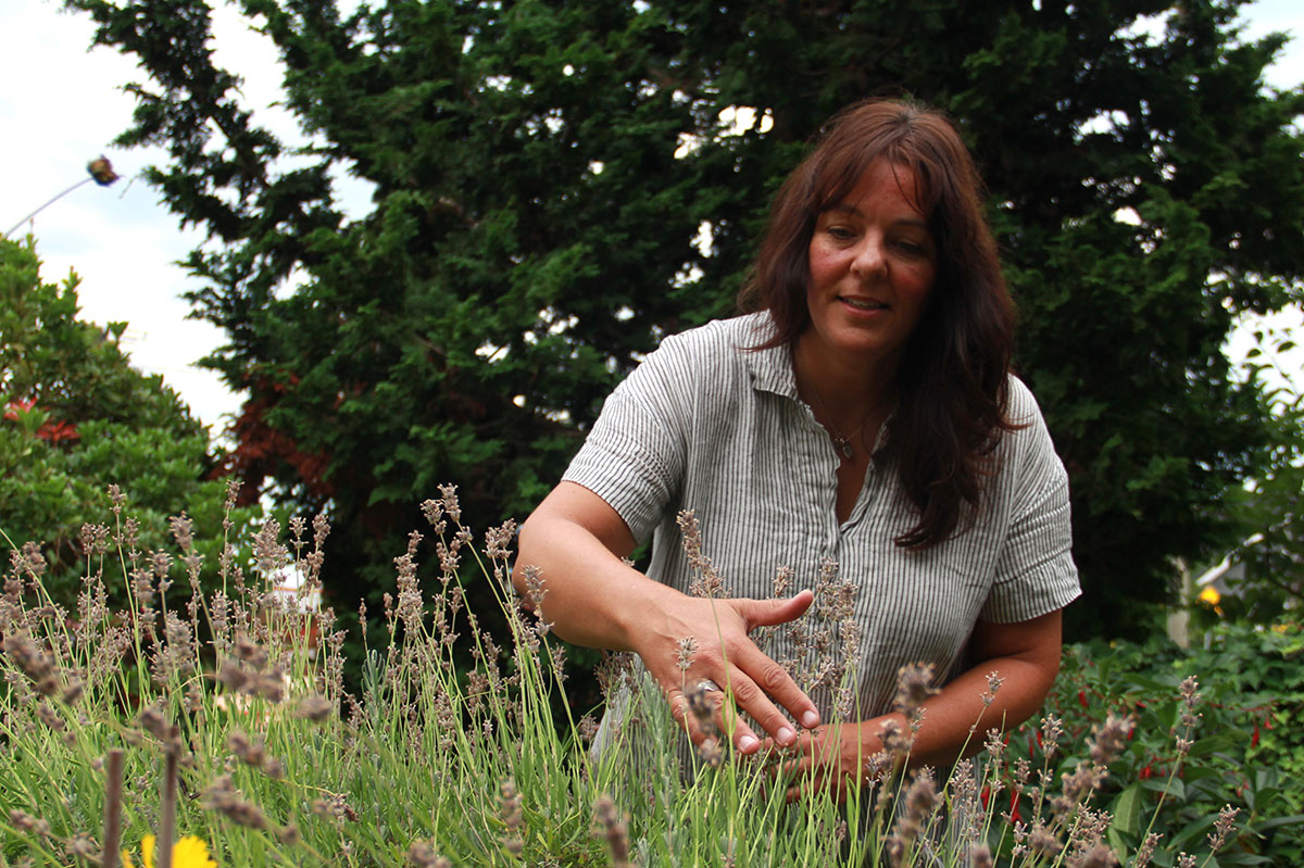 Genevi&egrave;ve Blanchet, a woman with long brown hair wearing a white and grey striped shirt, picks flowers.