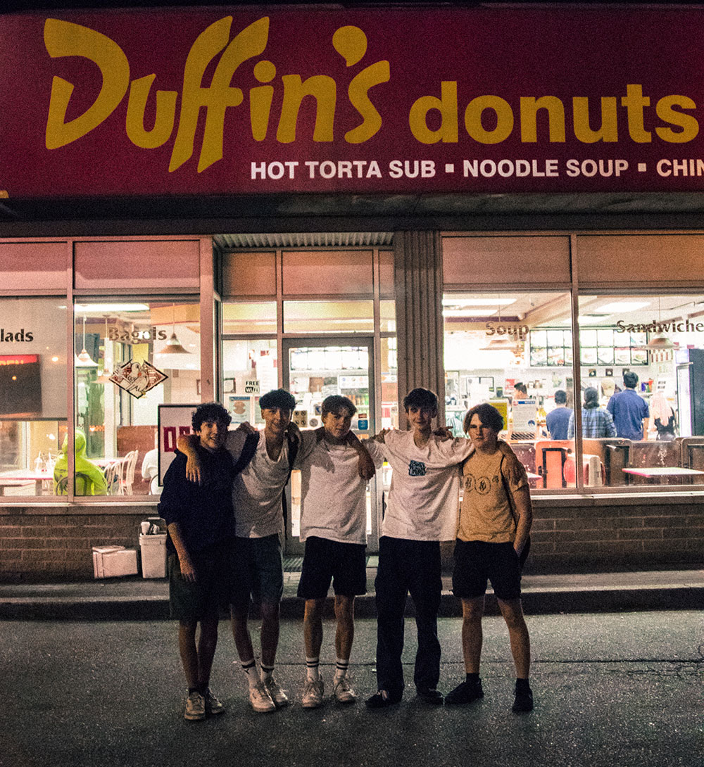 Five teenage boys stand outside Duffin’s. They are standing in a line, their arms across each other’s shoulders.