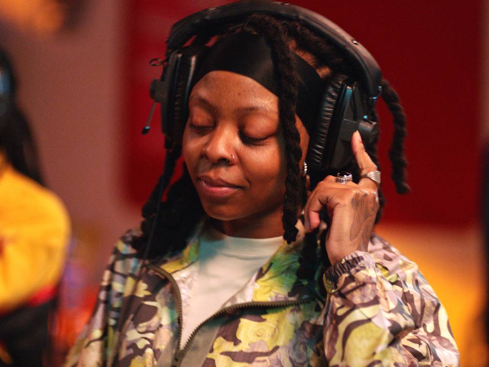 Two stacked images depict two rappers performer. In the top image, Yousseff Joker is wearing headphones, holding a microphone in his left hand, and smiling. In the bottom image, TrueMendous is holding a headphone to her ear, looking down, listening and smiling softly. 