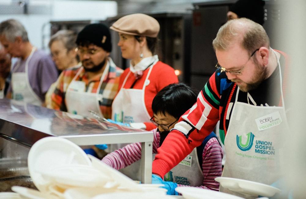 People wearing aprons, one saying Union Gospel Mission, serve food.