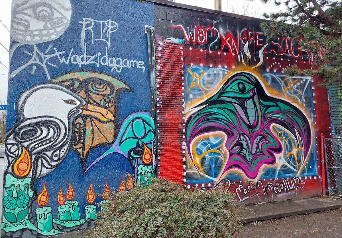 A &ldquo;Womxn are sacred&rdquo; mural stands to the right of a blue mural with silver stylized script that reads &ldquo;RIP Wadzidagame;&rdquo; stylized turquoise memorial candles line the bottom of the mural.