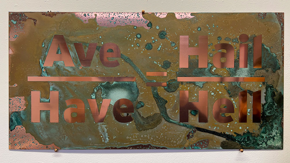 The words &ldquo;Ave&rdquo; over &ldquo;Have&rdquo; on the left, &ldquo;Hail&rdquo; over &ldquo;Hell&rdquo; on the right are in bronze san serif text laid over a polished copper plate oxidized with urine.