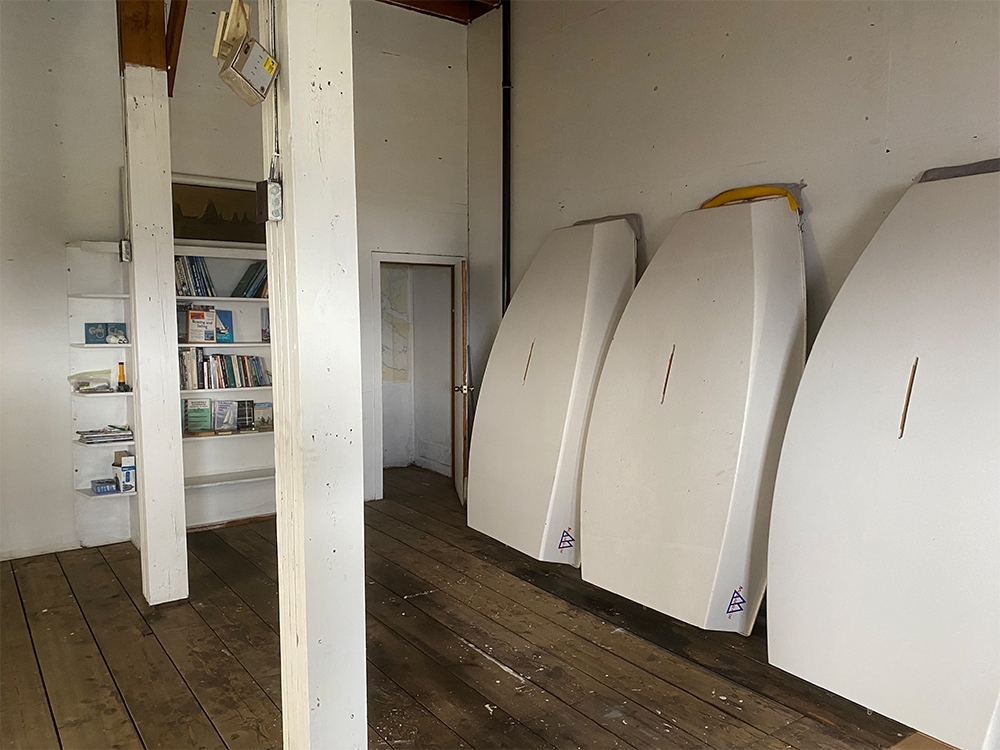 Three white small sailing shells are lined up against the wall. The room has high ceilings. A bookshelf is visible beyond two support beams. 