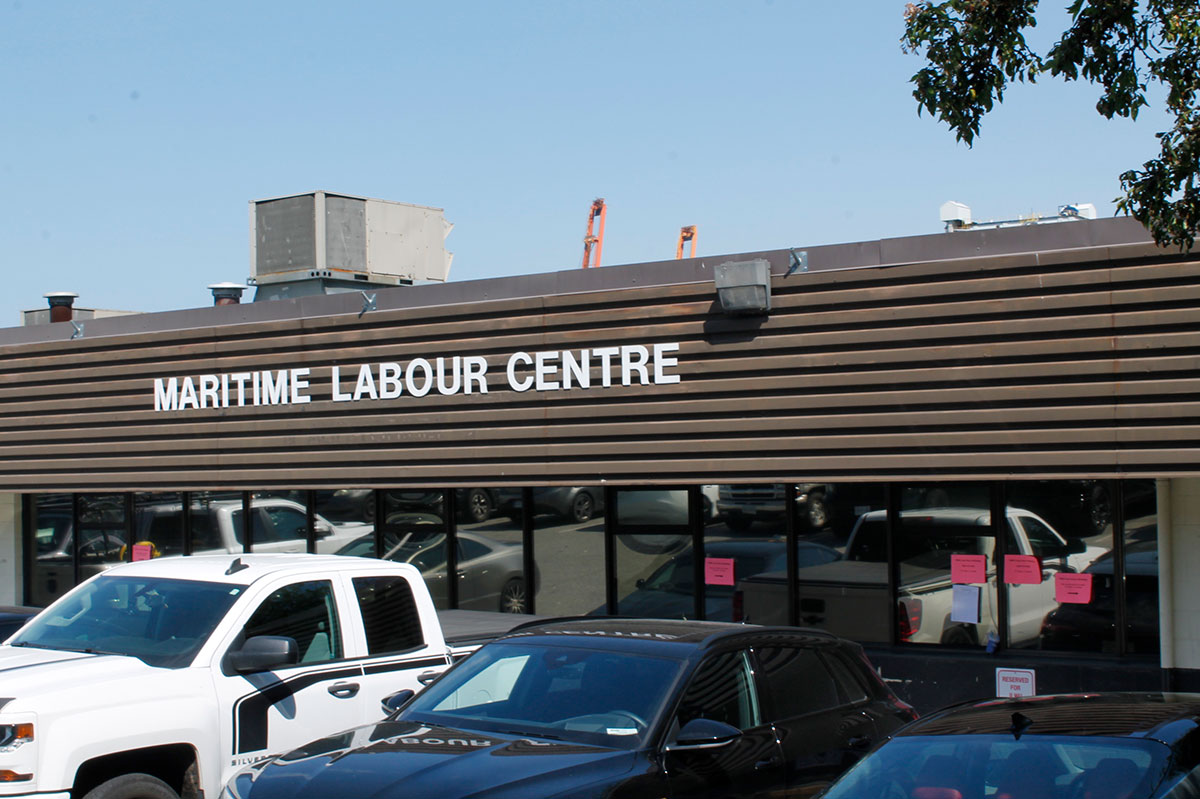 Cars are parked outside the exterior of Maritime Labour Centre, which features white lettering on a brown corrugated metal background.