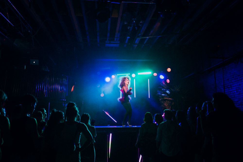 A performer in a pink dress is illuminated with blue-hued lights and dances before a large audience.
