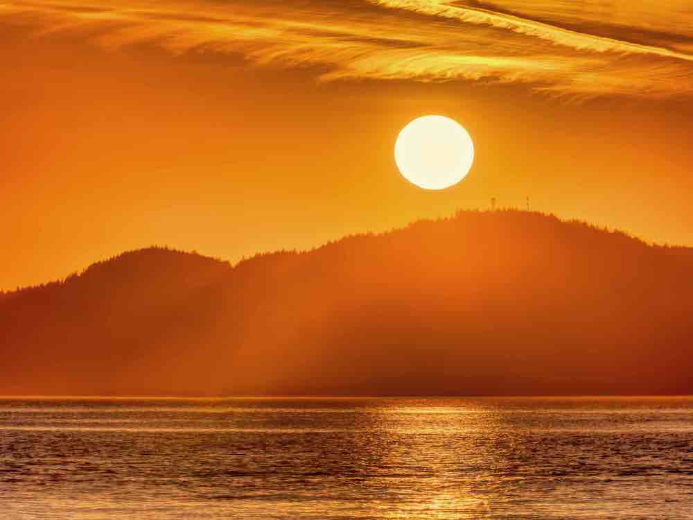 The Pacific Ocean and a mountain range against an orange sky at sunset, as shot from a beach.
