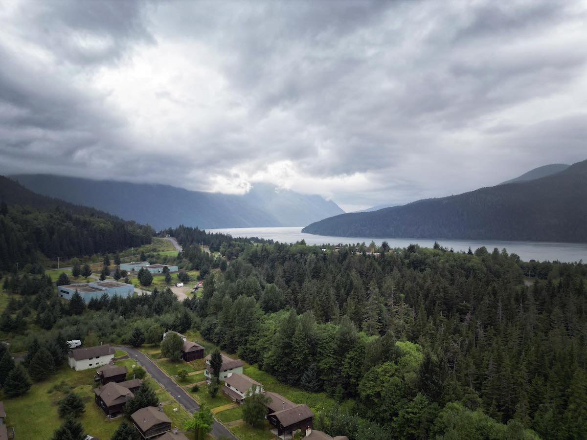 An aerial photo showing rows of residential homes and two larger buildings with a coastal fjord beyond.