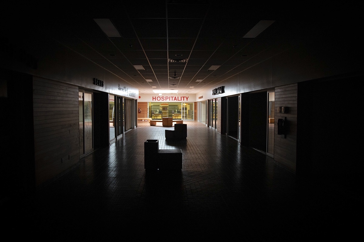 A sign over an empty store at the end of a darkened corridor says &ldquo;hospitality&rdquo; in all caps.