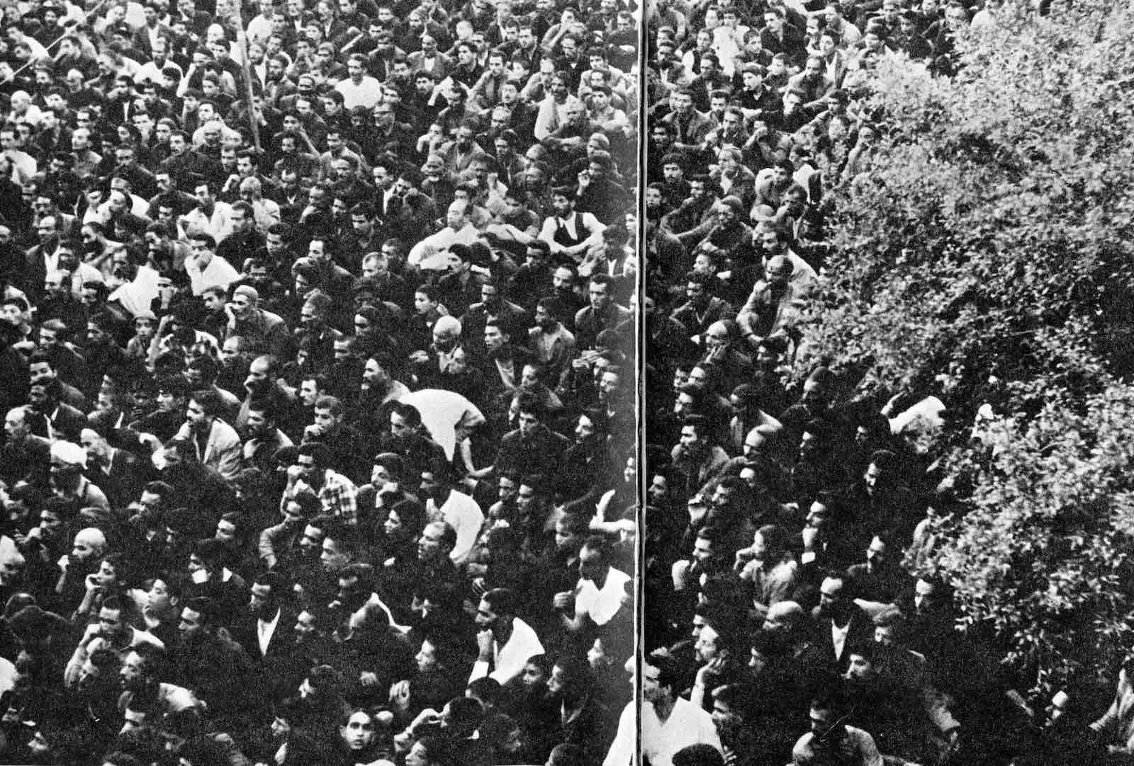 A large-format black and white archival image of a large crowd of men seated in an outdoor space.
