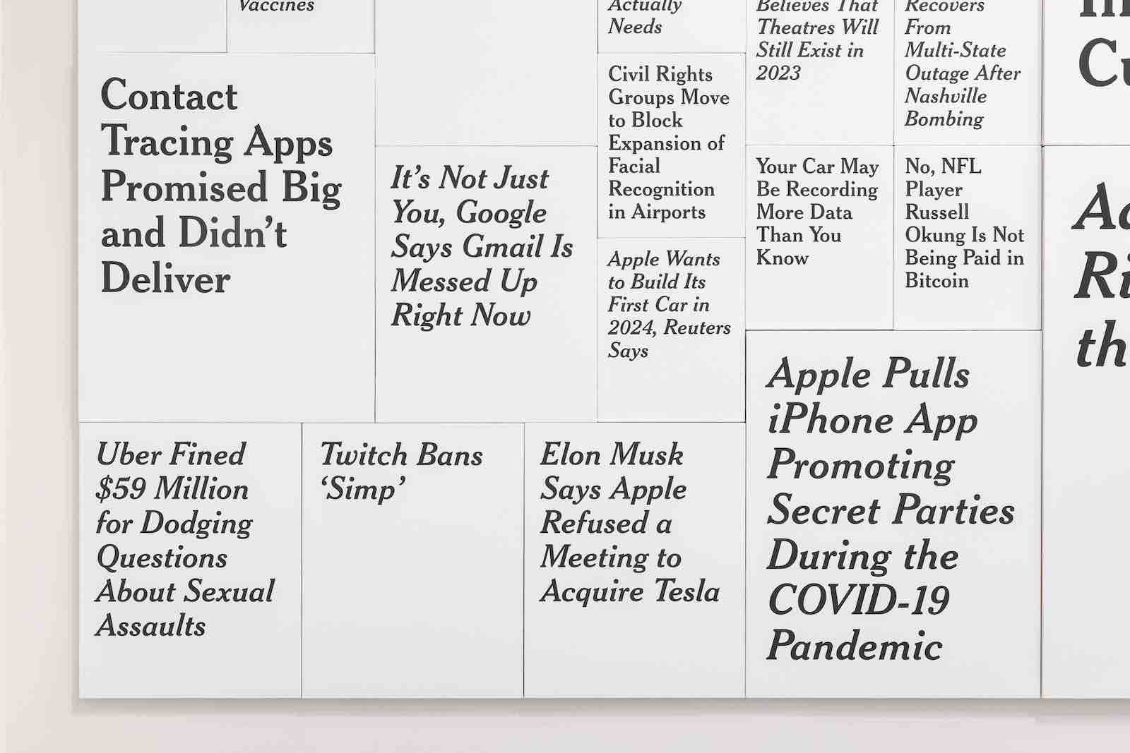 A collage of black and white news headlines in large sans serif typeface are arranged together on a gallery wall.