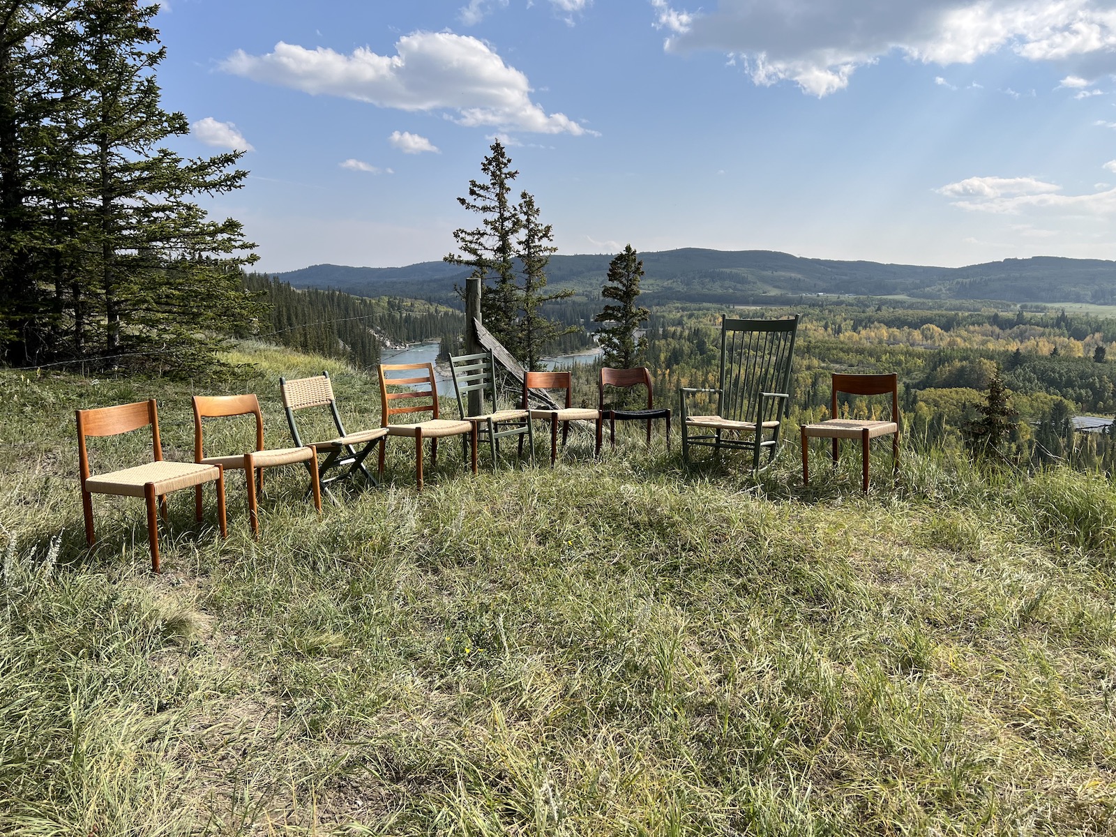 A row of mid-century modern chairs in front of a beautiful grassy landscape with a river in the back.