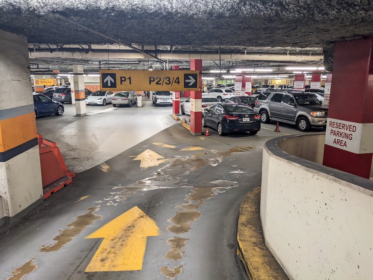 A parking garage entrance curves around a bend. Tire tracks have worn the concrete floor.