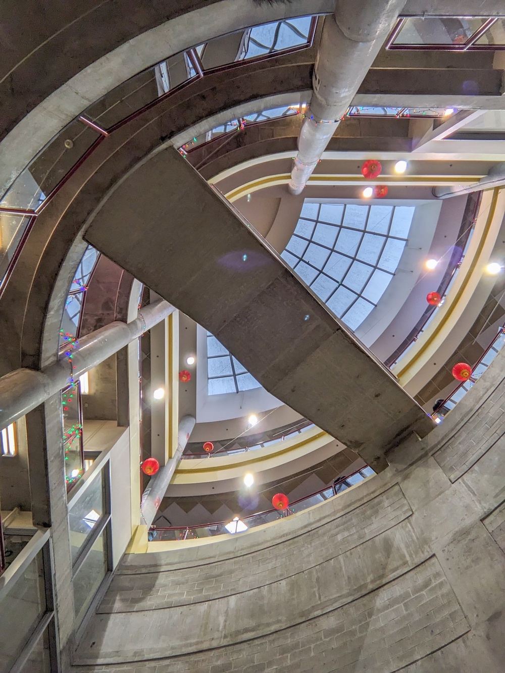 A glass roof is visible looking up from the bottom of the lightwell. The concrete bottom of a stairway that crosses the chasm bisects the lightwell.
