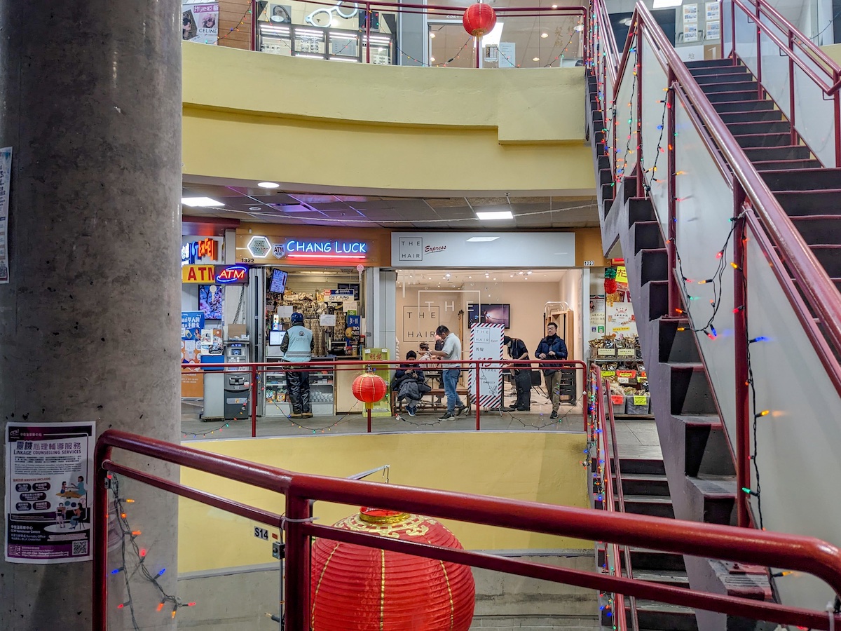 A few businesses are visible beyond the flight of stairs that bisects the lightwell. One sign reads, 'The Hair Express.' Another reads, 'Chang Luck.'