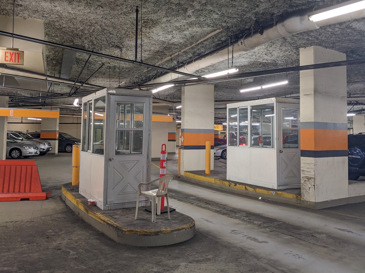 Empty, narrow toll booths sit on two concrete islands. They don&rsquo;t stretch to the roof of the parking garage. An empty plastic lawn chair sits in front of one of them.