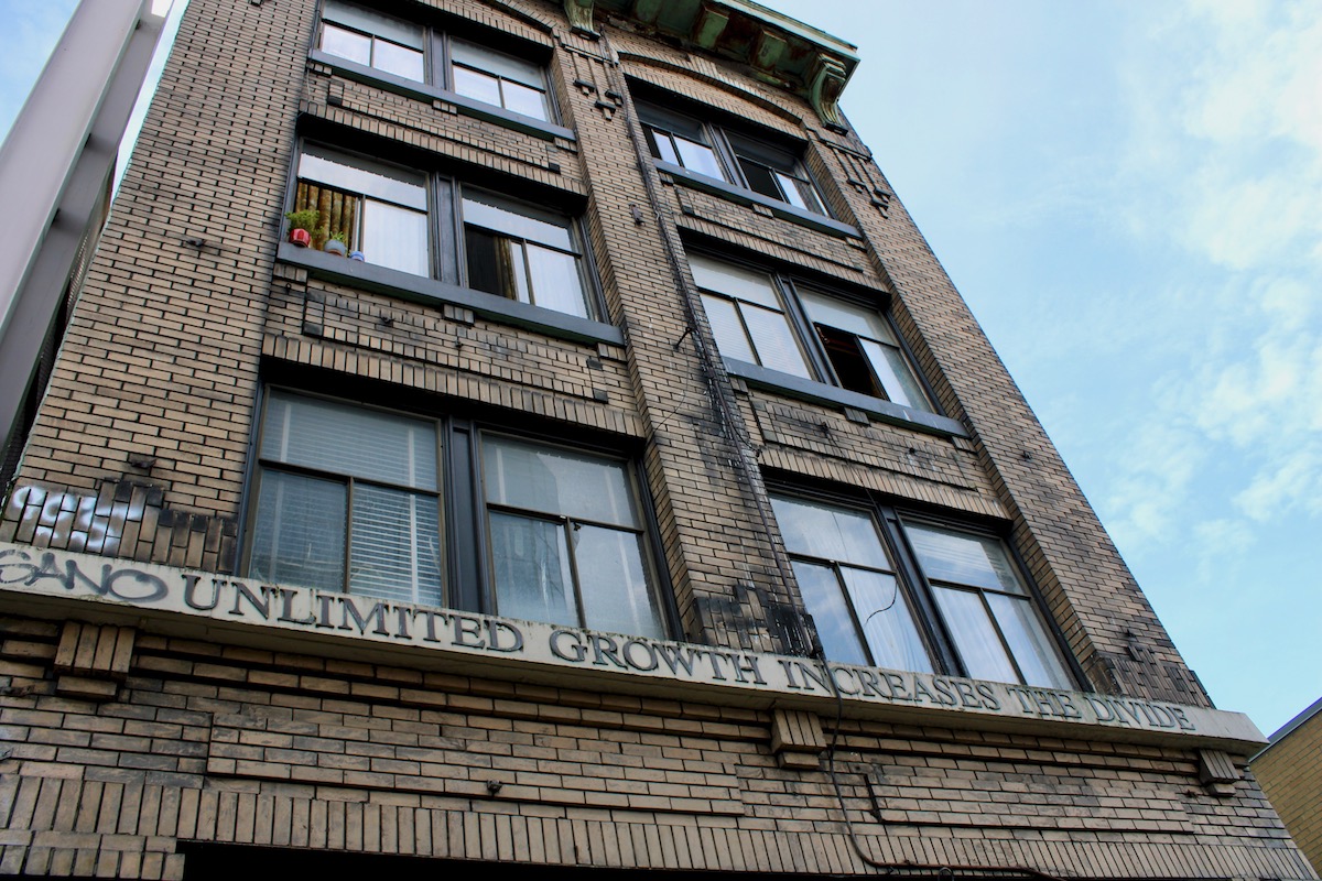 A photo shows the bottom two floors of the Del Mar building. Letters above the door read, 'Unlimited Growth Increases the Divide.'