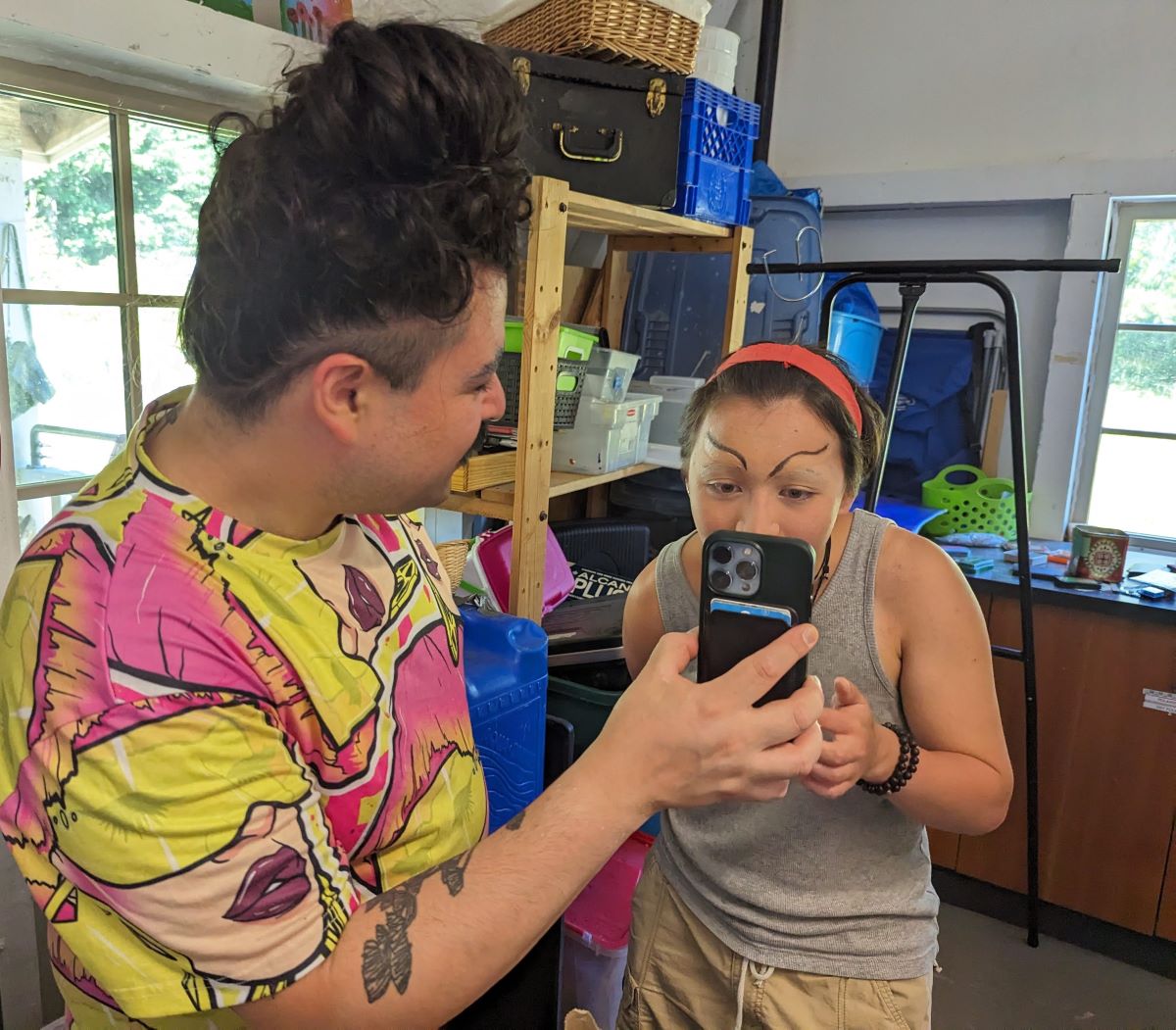 A medium-skin tone person faces away from the camera, showing a younger medium-light skin tone person their phone.