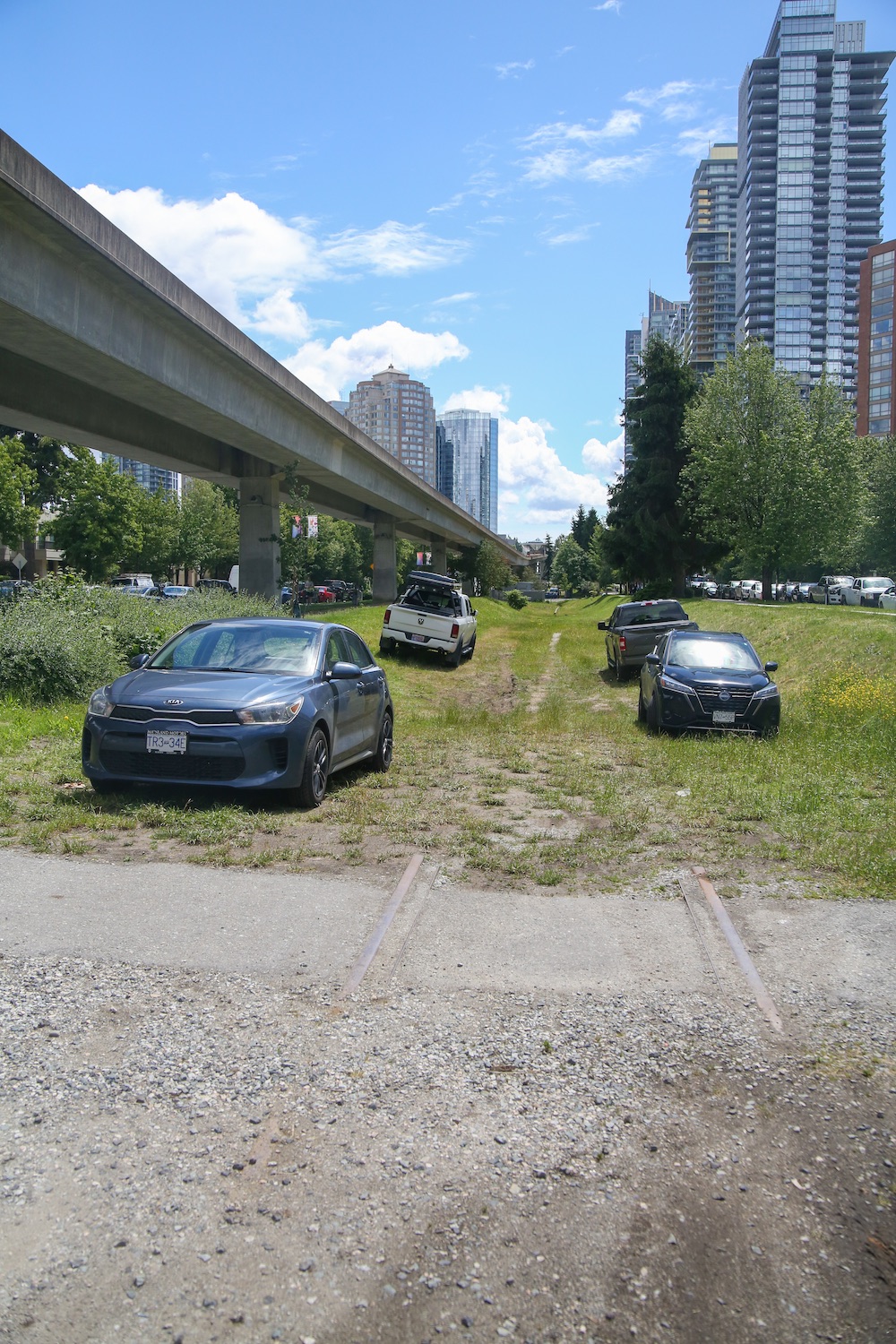 Four cars are parked to the side of the old interurban tracks, in bumpy, slightly angled grass.