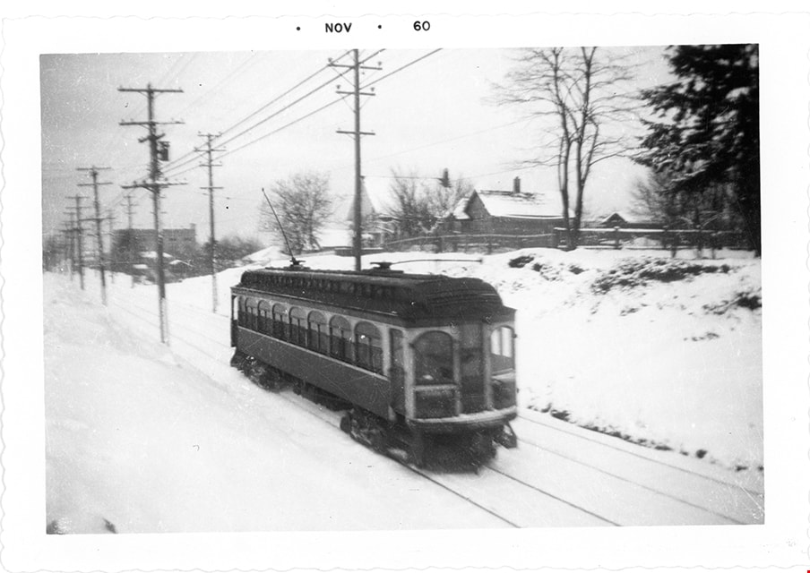 A black and white photo of a trolley zooming down the tracks of the interurban on a snowy day.