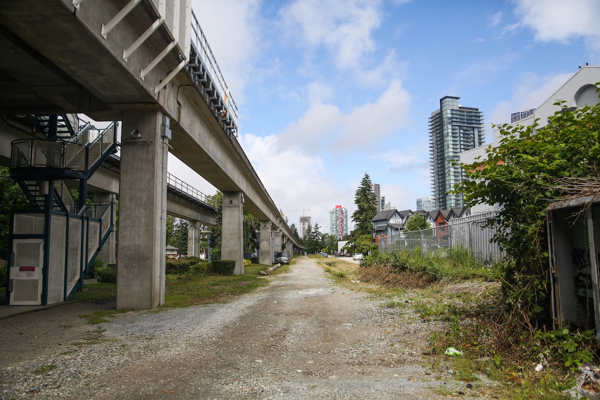An empty, gravel-covered grade runs parallel to the SkyTrain.