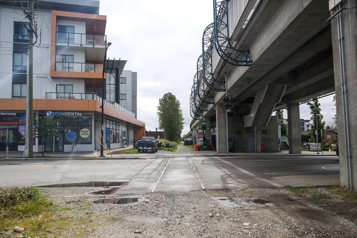 Rail tracks are visibly embedded in a road. The SkyTrain runs adjacent, overhead.