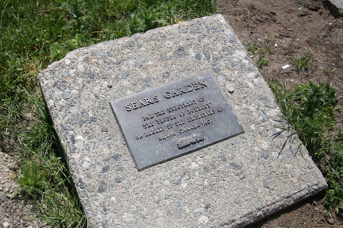 A plaque on the ground reads, 'Sears Garden: for the enjoyment of the people of Burnaby on behalf of the employees of Sears Canada Inc.'
