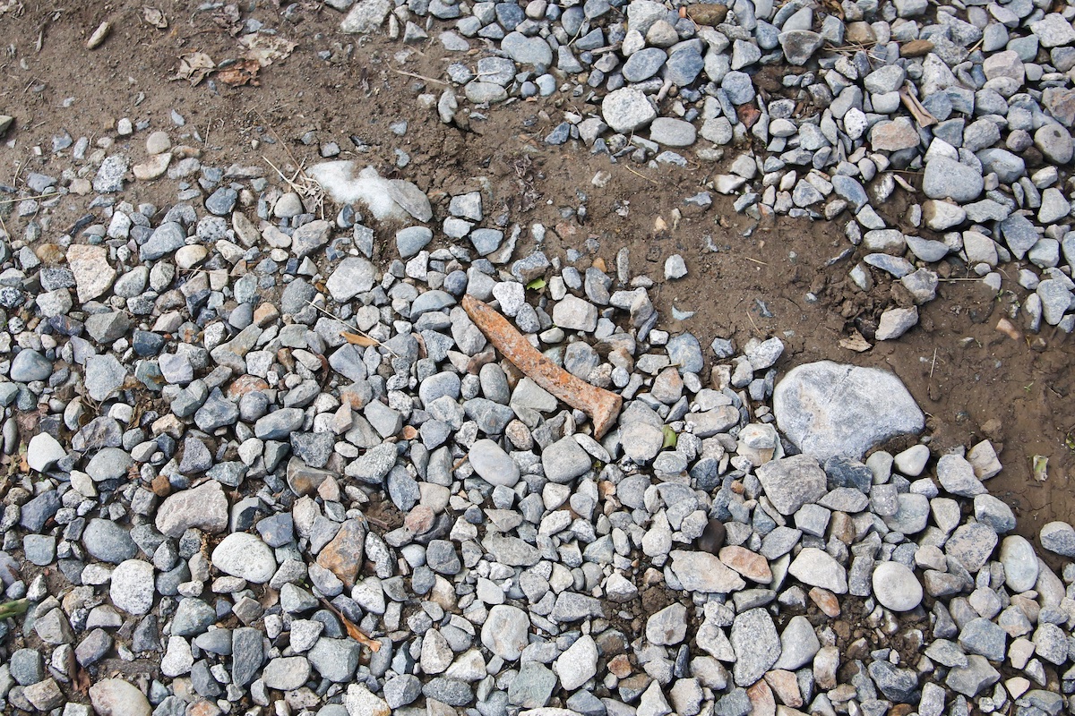 A rusty metal rail spike amidst large chunks of gravel.