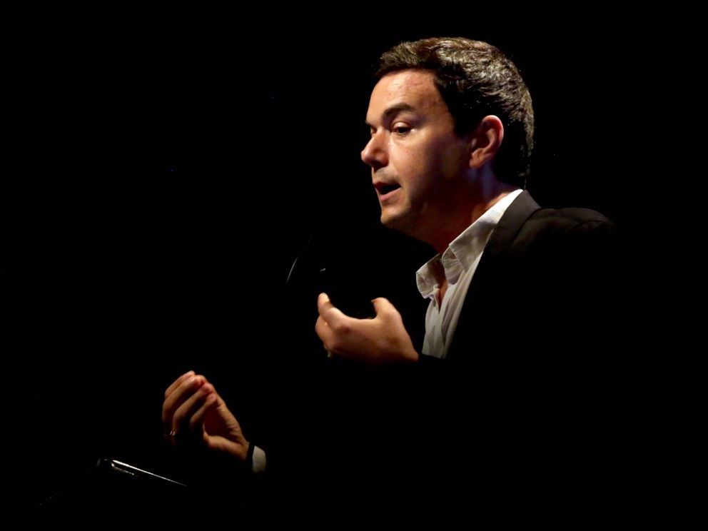 A white man of young middle age with brown hair gestures as he gives a talk.