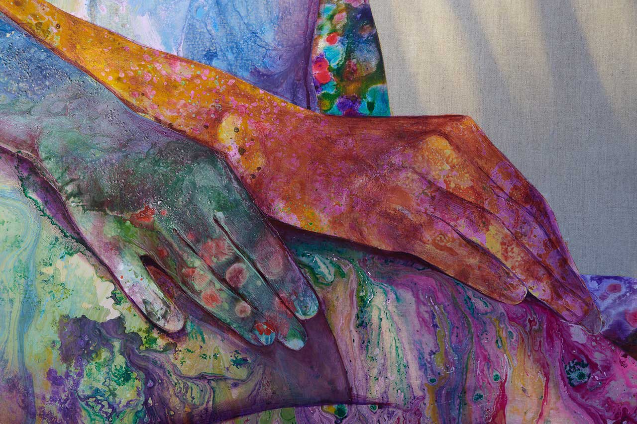 A colourfully painted wooden frame features a pair of hands resting on a lap in blue, green, orange and purple shades that produce a cosmic, liquified effect. 