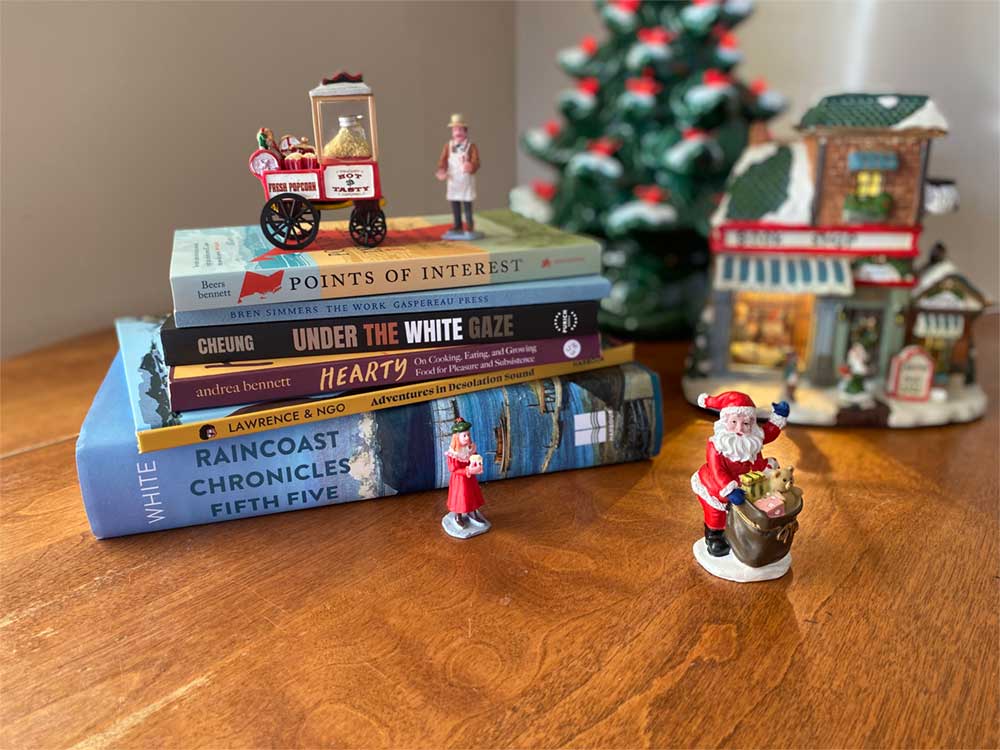 A small Christmas scene shows a stack of books amidst some miniatures, a ceramic light-up bookshop and a ceramic Christmas tree.