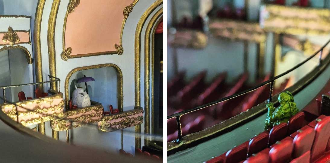 The interior of a miniature cinema features a small grey figurine of Totoro, a large round grey cat, in the balcony, and a slimy green figure in the seats facing the stage.