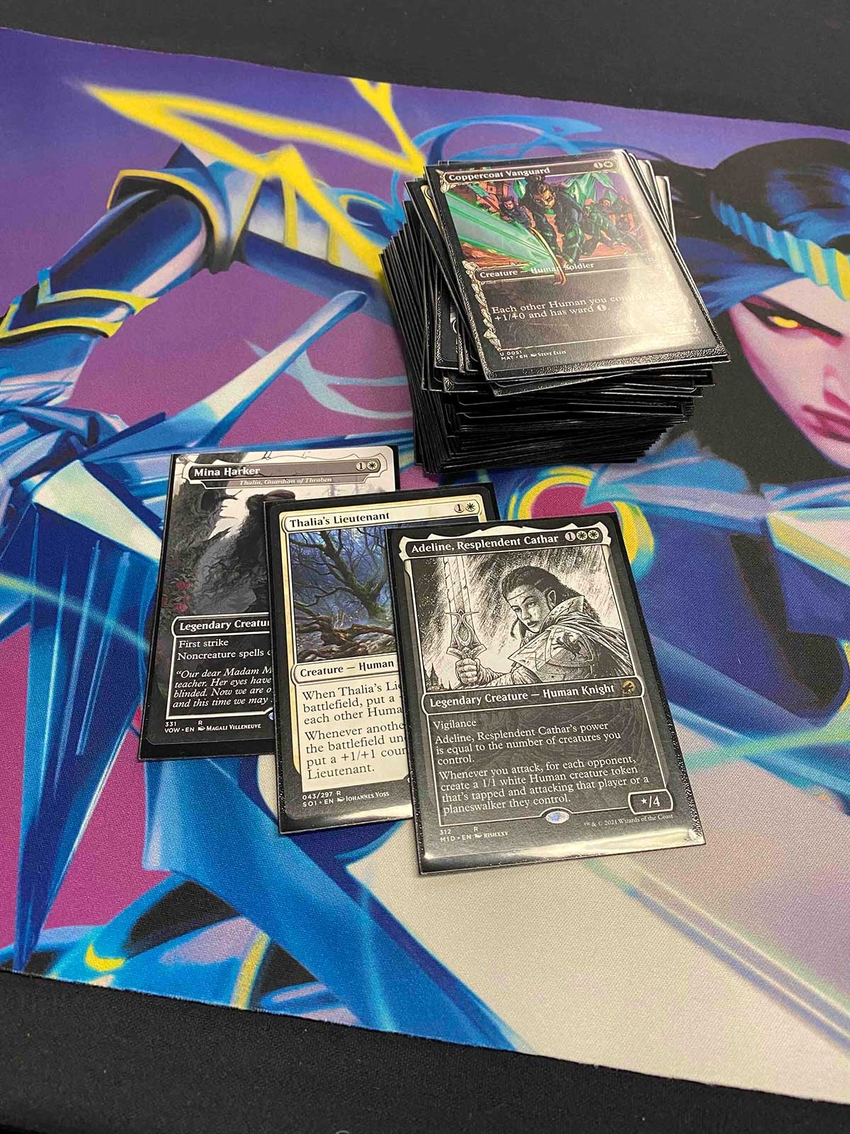A set of colourful Magic: The Gathering cards sits on a colourful cardboard mat featuring a colourful graphic with purple, blue and grey.