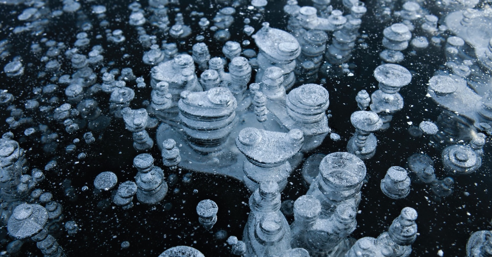 Rows of short stacks of round grey stones stand against a black surface.