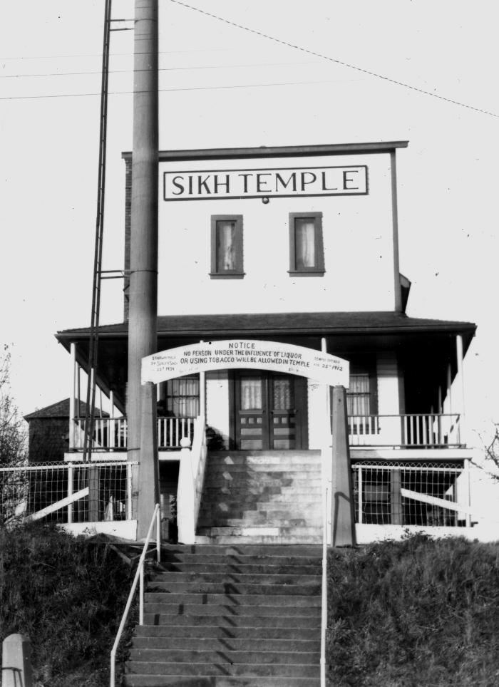 A black and white historical photo shows the gurdwara. It has an arched sign reading 'Sikh Temple.'