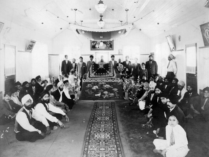 A black and white photo shows about 40 people sitting in the prayer hall.