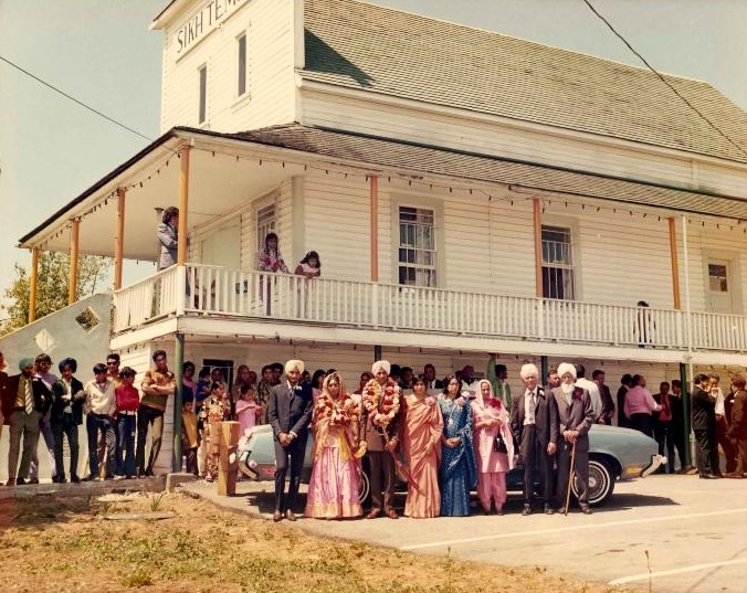 A vintage colour photo from a wedding. Lots of people are standing around a powder-blue car.