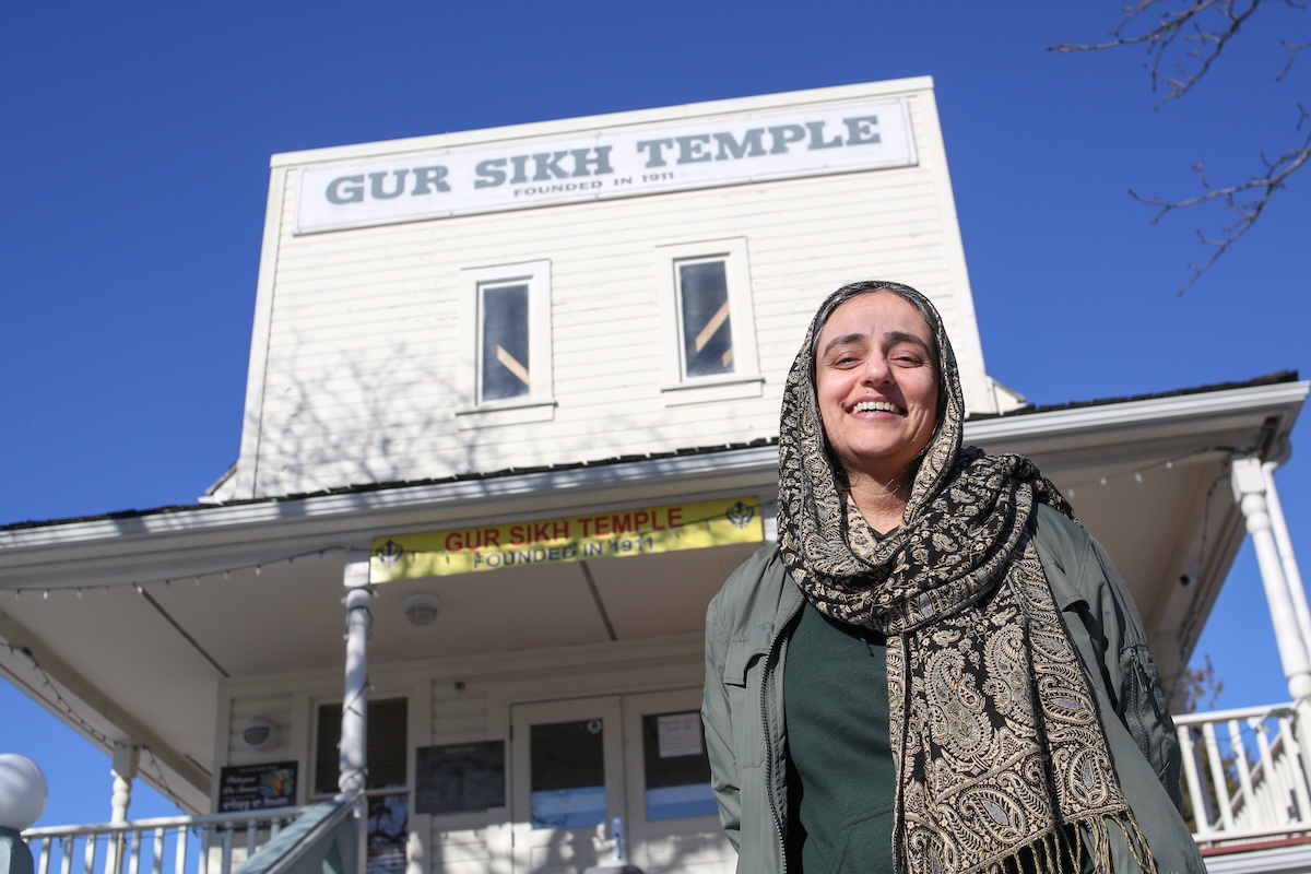 Sharanjit Kaur Sandhra, a middle-aged woman with medium skin tone, stands in front of the gurdwara.
