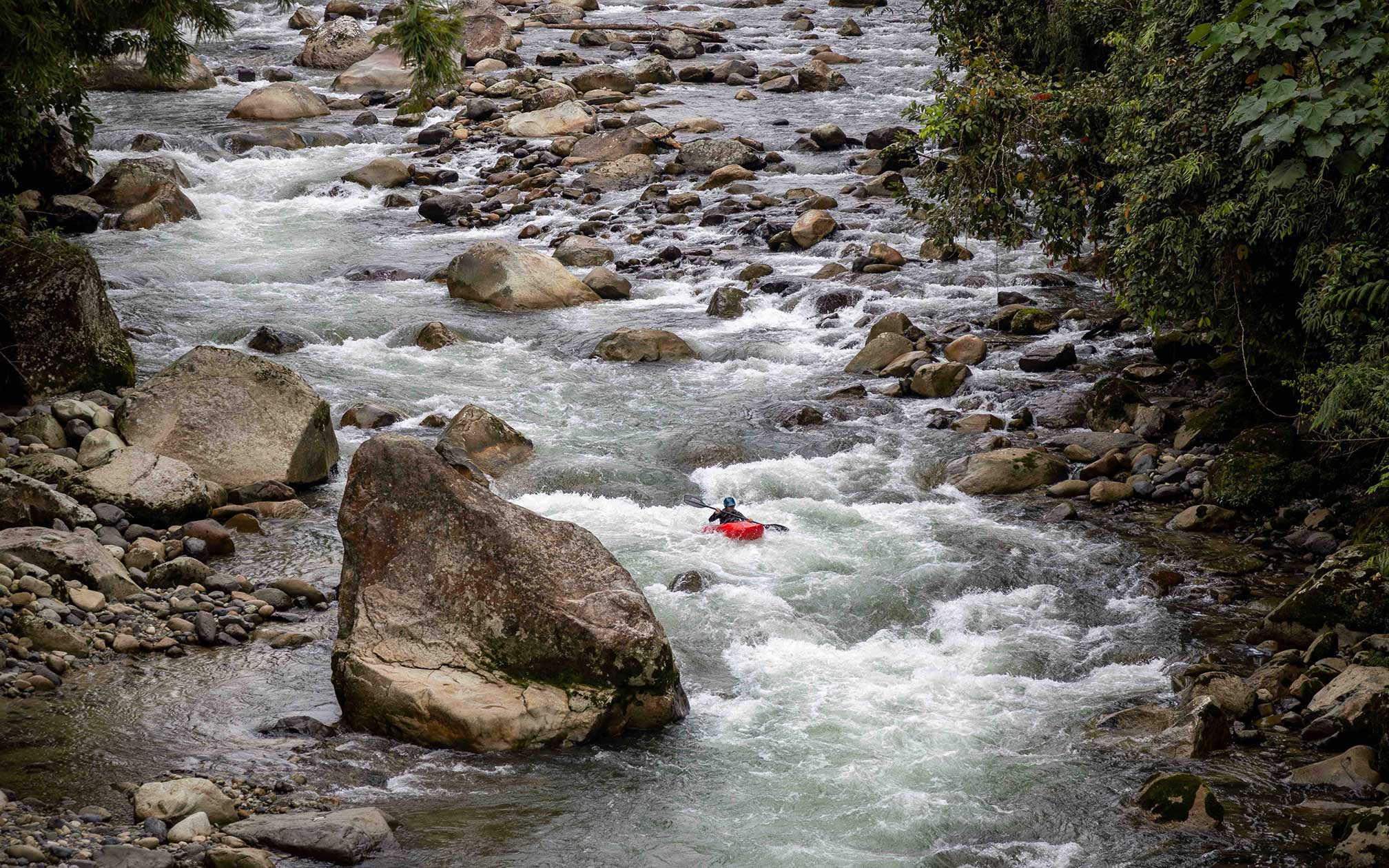 A young woman in a red kayak paddles down rocky rapids.