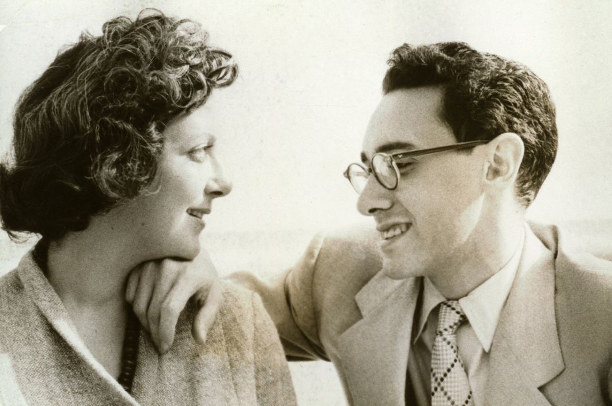 A black-and-white photograph depicts a couple in the 1950s. Marcella Hazan, left, has short dark wavy hair and a pale skin tone. She is wearing a tweed jacket and looking towards. Victor Hazan, right. He has short dark hair, glasses and is wearing a light suit and tie. He places a hand on Marcella&rsquo;s shoulder.