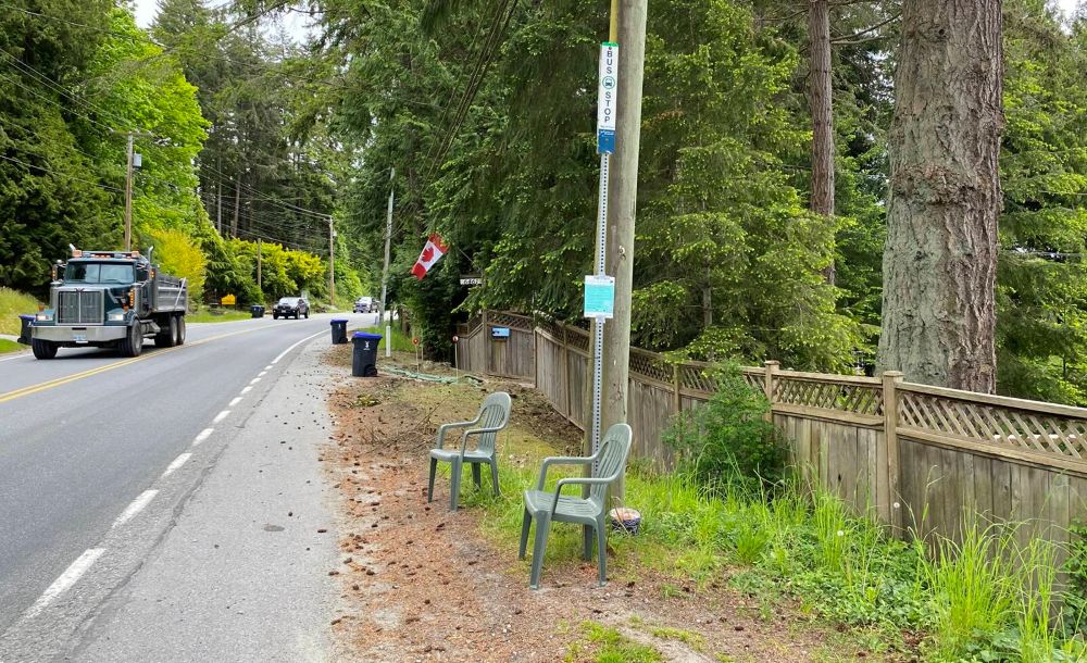 Two green lawn chairs straddle a bus stop on the side of the Sunshine Coast highway. 