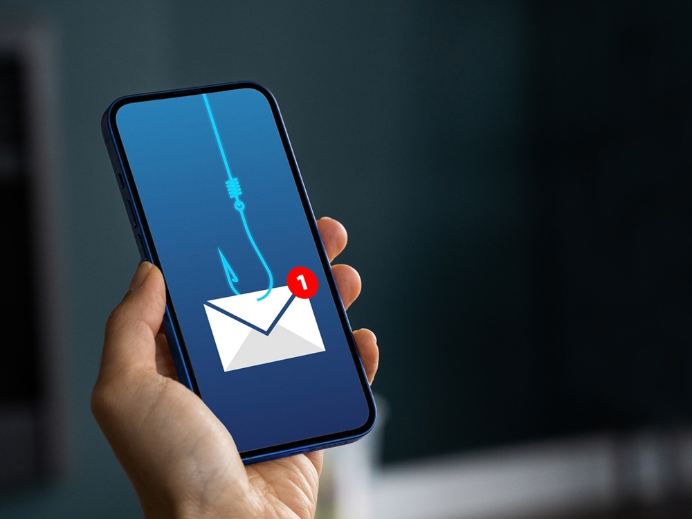 A hand holds a cellphone. The cellphone displays an illustration: a fishing hook through an email icon.