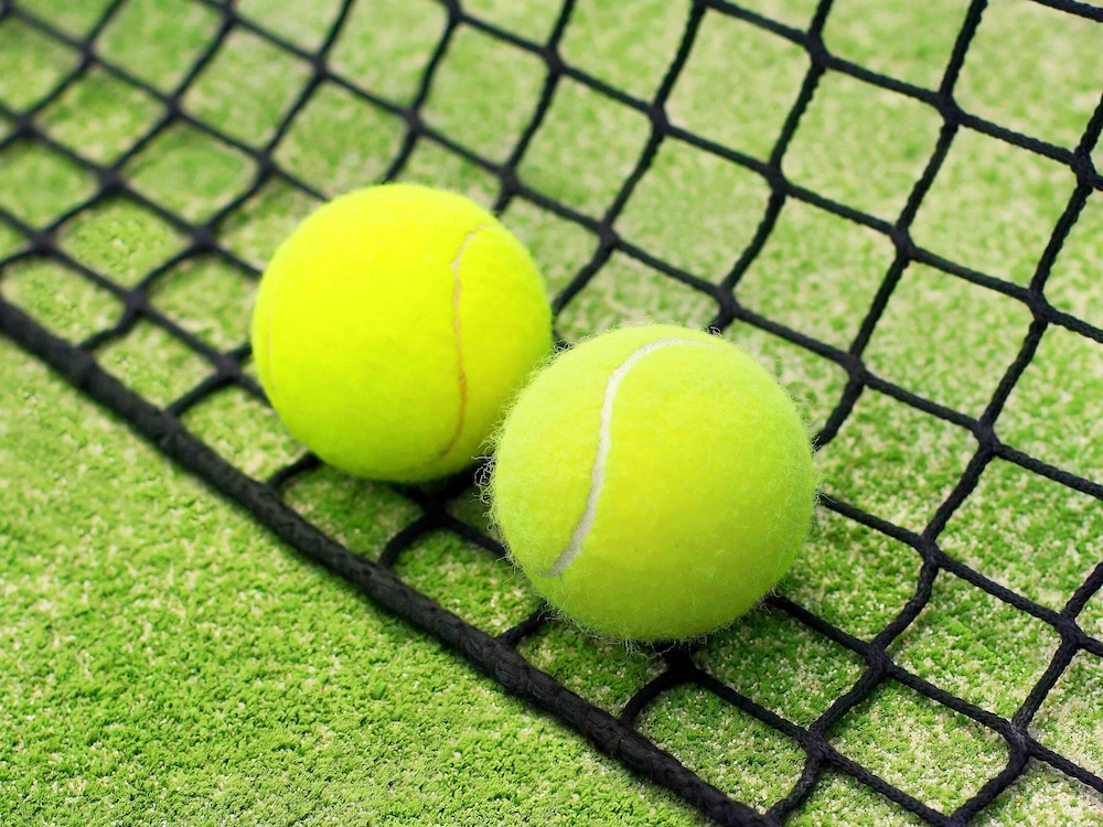 A pair of neon green tennis balls rests on a black net against a green background.