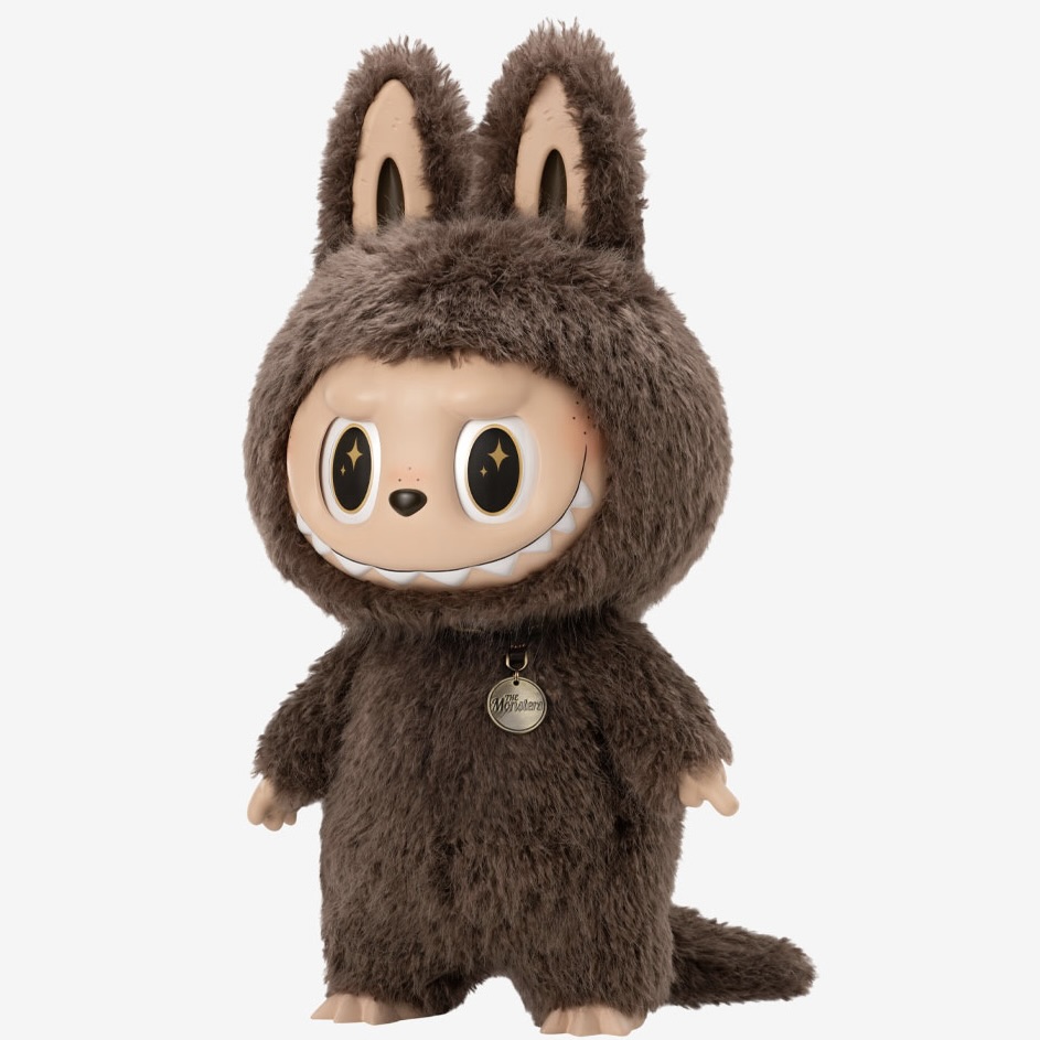 A brown furry Labubu doll stands against a white background. It has dark brown fur and a vinyl face in a light flesh tone. It has large cartoon eyes, sharp teeth like a cartoon monster, and two pointy ears.