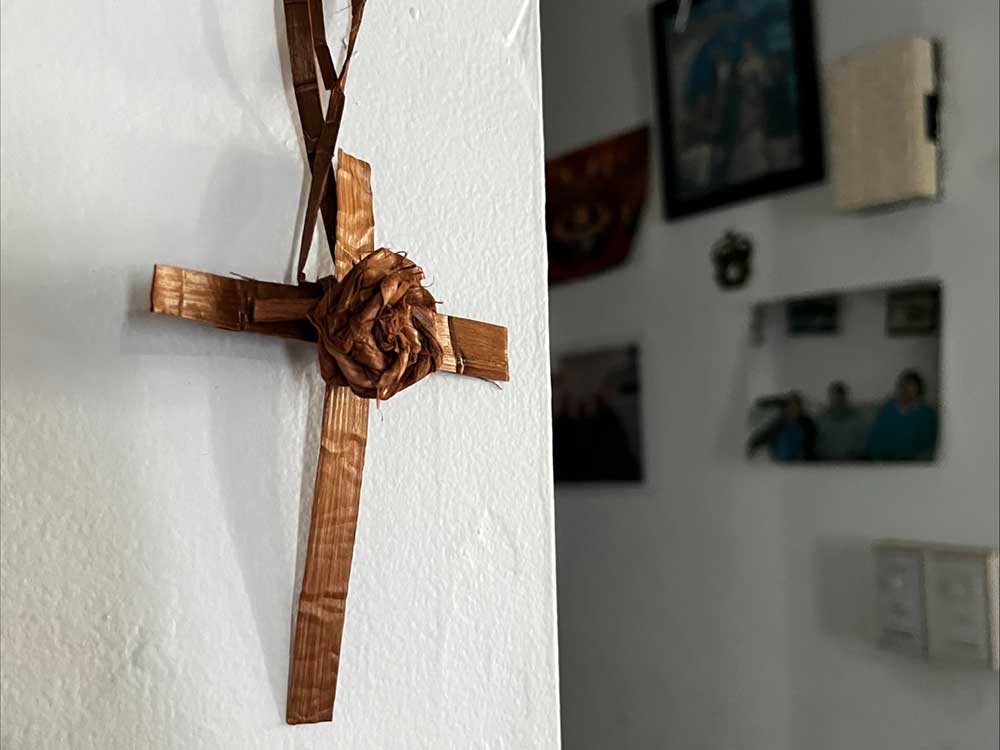 A cedar cross with a cedar flower at the centre hangs on a white wall.