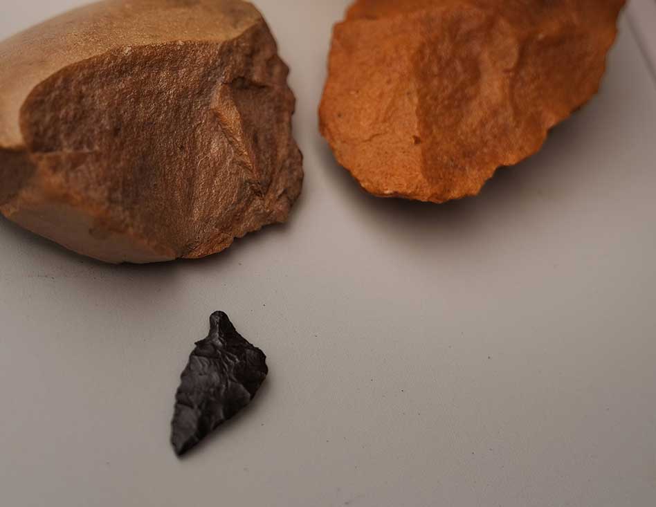 Two terra-cotta-coloured rocks are assembled on a white tabletop at the top of the frame, and a dark arrow-shaped piece of stone is at the bottom of the frame.