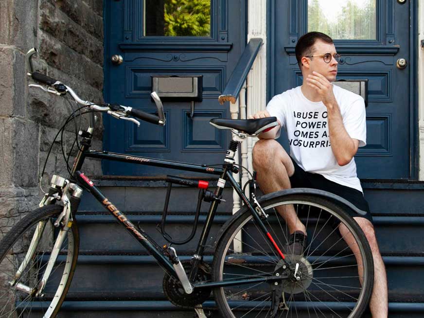 Alex Manley sits on the steps of a Montreal apartment building with a bike in front of them.